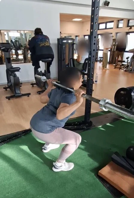 Aluna a fazer agachamento com barra